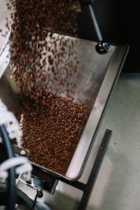 Close-up of coffee beans being poured into a roasting machine, showcasing industrial coffee production.